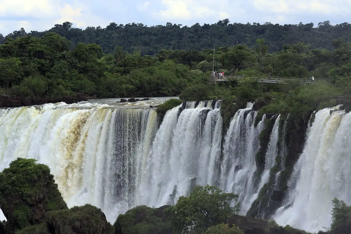 The wide San Martín waterfall on the Argentine side, with visitors on the Upper Circuit viewpoint above the falls and rainforest behind